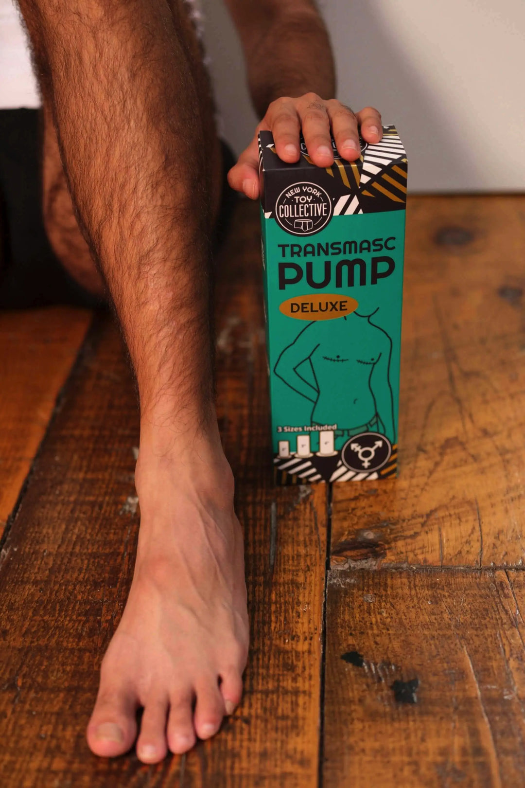 Person holding a box labeled 'Transmasc Pump Deluxe' on a wooden floor.
