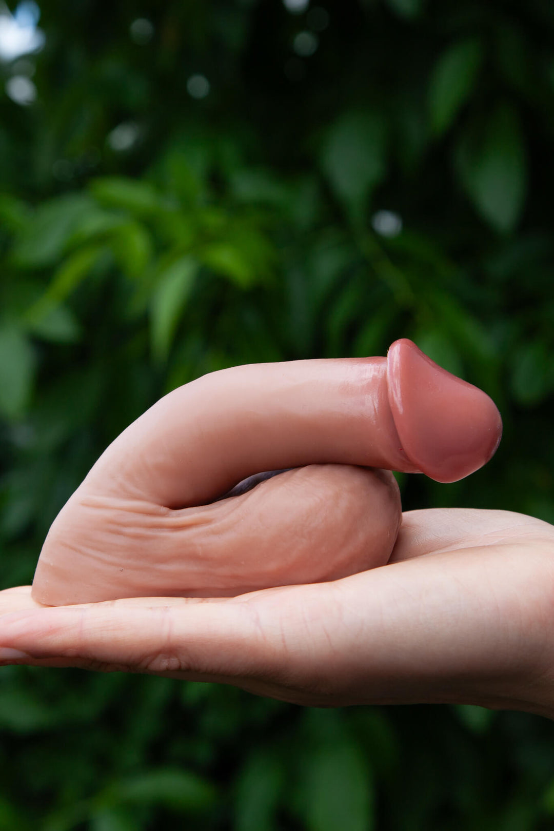 Hand holding a small pink object against a blurred green background