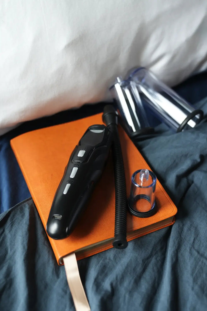 Black electronic device on an orange notebook with a clear glass container on a bed