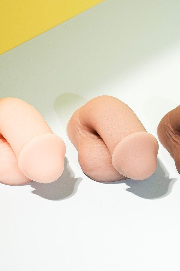 Three silicone finger-like objects in different colors on a white surface with a yellow background.