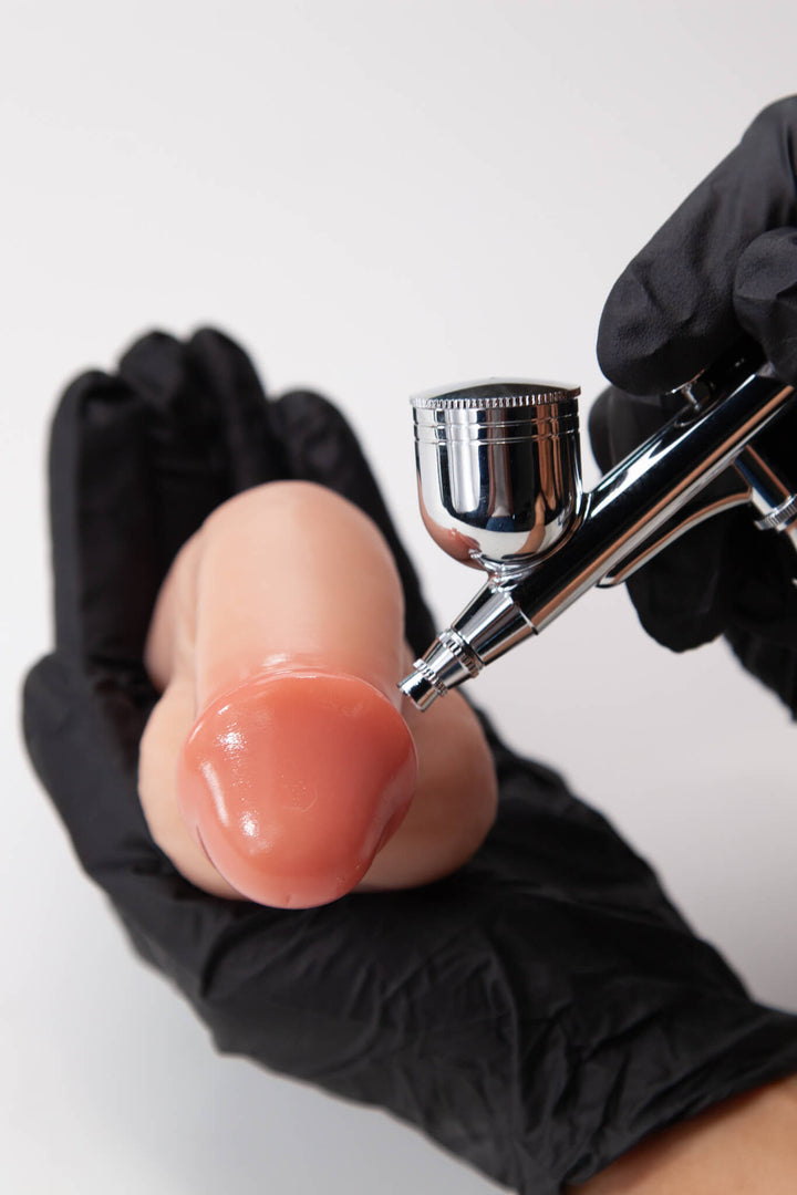 Airbrush being used on a silicone mold of a prosthetic against a white background