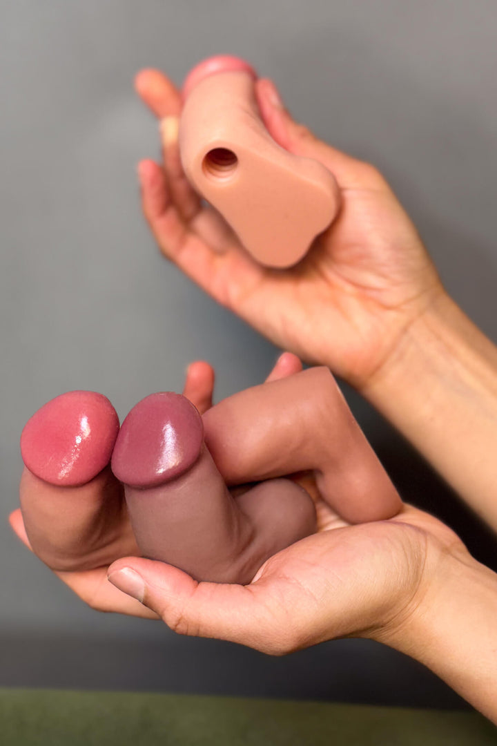 Hands holding pink silicone breast forms against a neutral background
