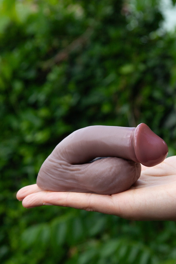 Hand holding a silicone mold shaped like a prostheticagainst a blurred green background